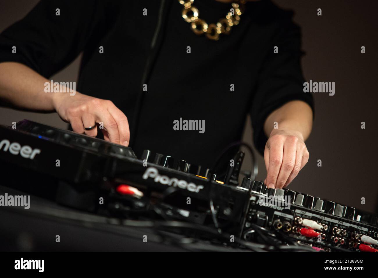 Set da festa DJ (disc jockey) con console di miscelazione Pionneer, maglietta nera e grande catena dorata. Primo piano di mani Foto Stock