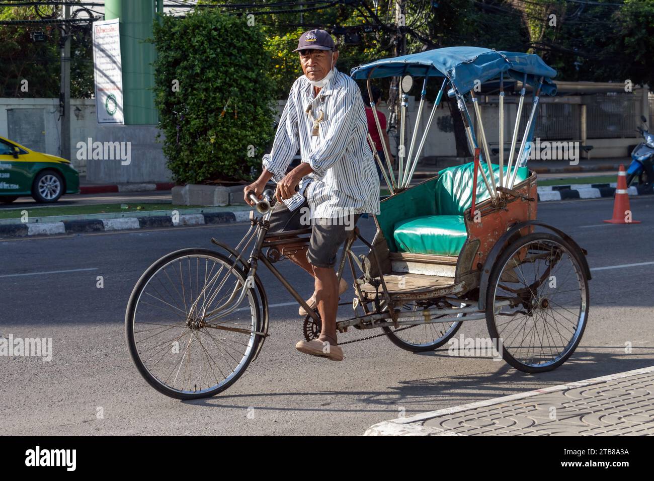 SAMUT PRAKAN, THAILANDIA, 12 novembre 2023, Un uomo guida un triciclo per trasportare un passeggero in una strada cittadina Foto Stock