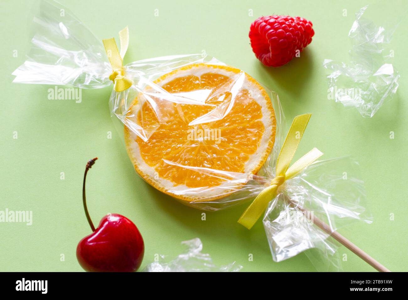 Fetta d'arancia su bastone e frutta avvolta in foglio, lecca lecca alla frutta, caramelle, sano sostituto per i dolci, concetto creativo Foto Stock