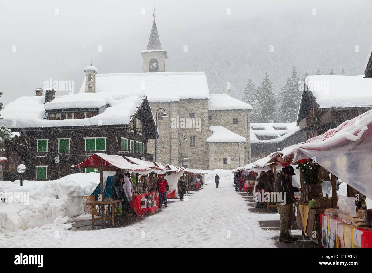 Onde fredde e neve in Europa in un villaggio alpino di montagna. La gente è alla ricerca di regali di Natale tra le bancarelle sotto la neve pesante, Macugnaga Italia Foto Stock