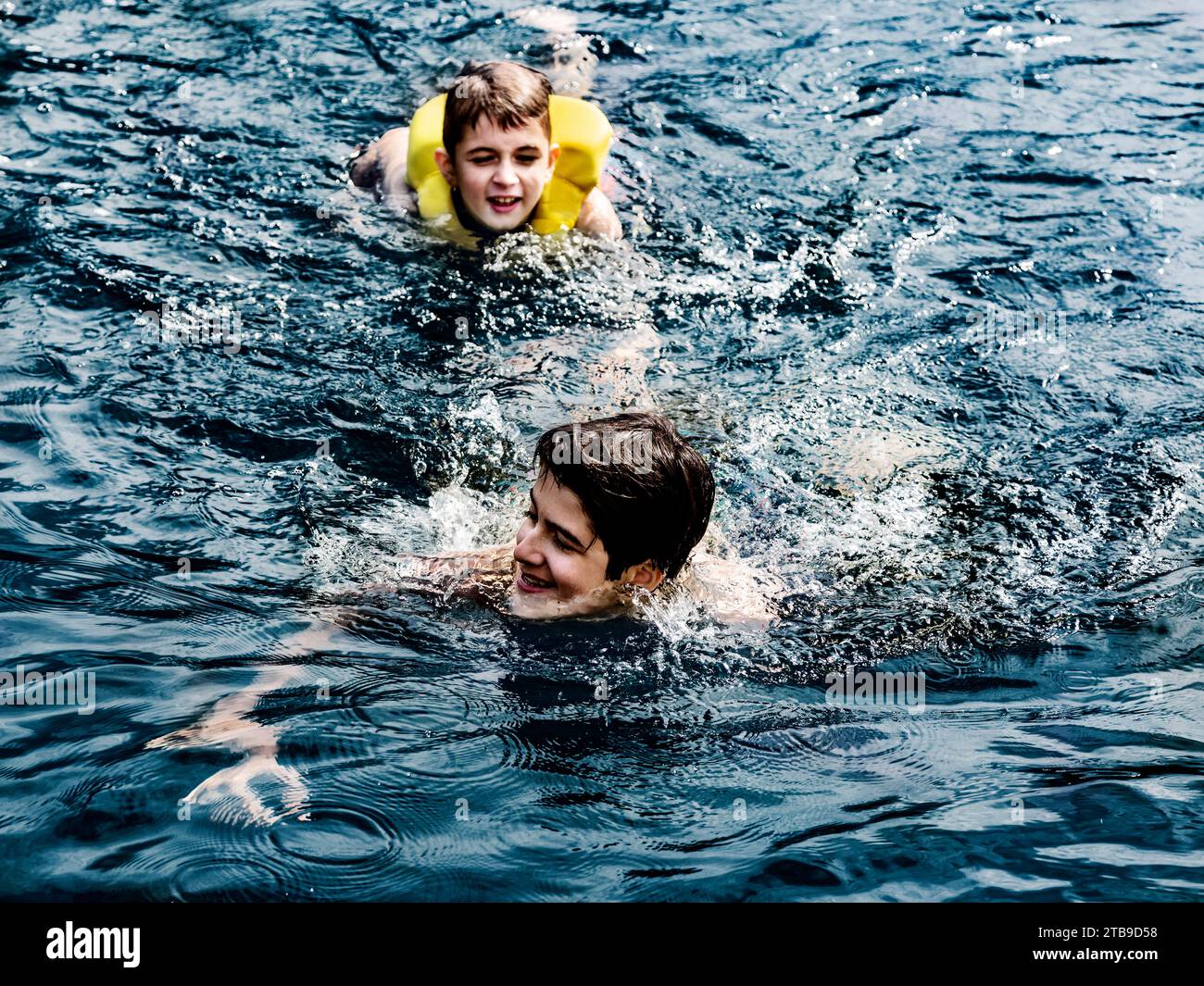 Due fratelli che nuotano in un lago mentre sono in vacanza e giocano nelle acque del lago Shuswap; British Columbia, Canada Foto Stock