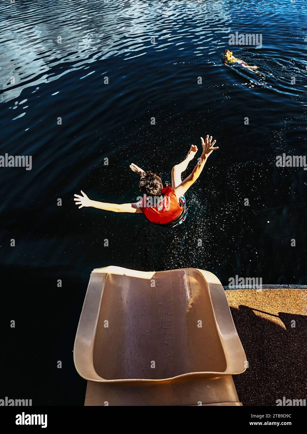 Boy vola a mezz'aria verso l'acqua dopo essere scivolato fuori dalla fine di uno scivolo d'acqua sul lago Shuswap; Columbia Britannica, Canada Foto Stock