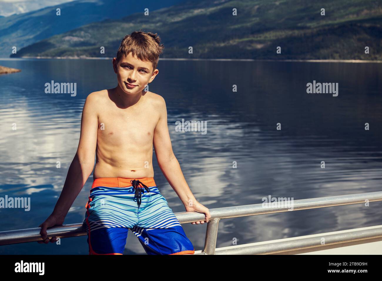 Ritratto di un giovane ragazzo seduto sul ponte di una casa galleggiante durante una vacanza mentre ancorato lungo la costa del lago Shuswap Foto Stock