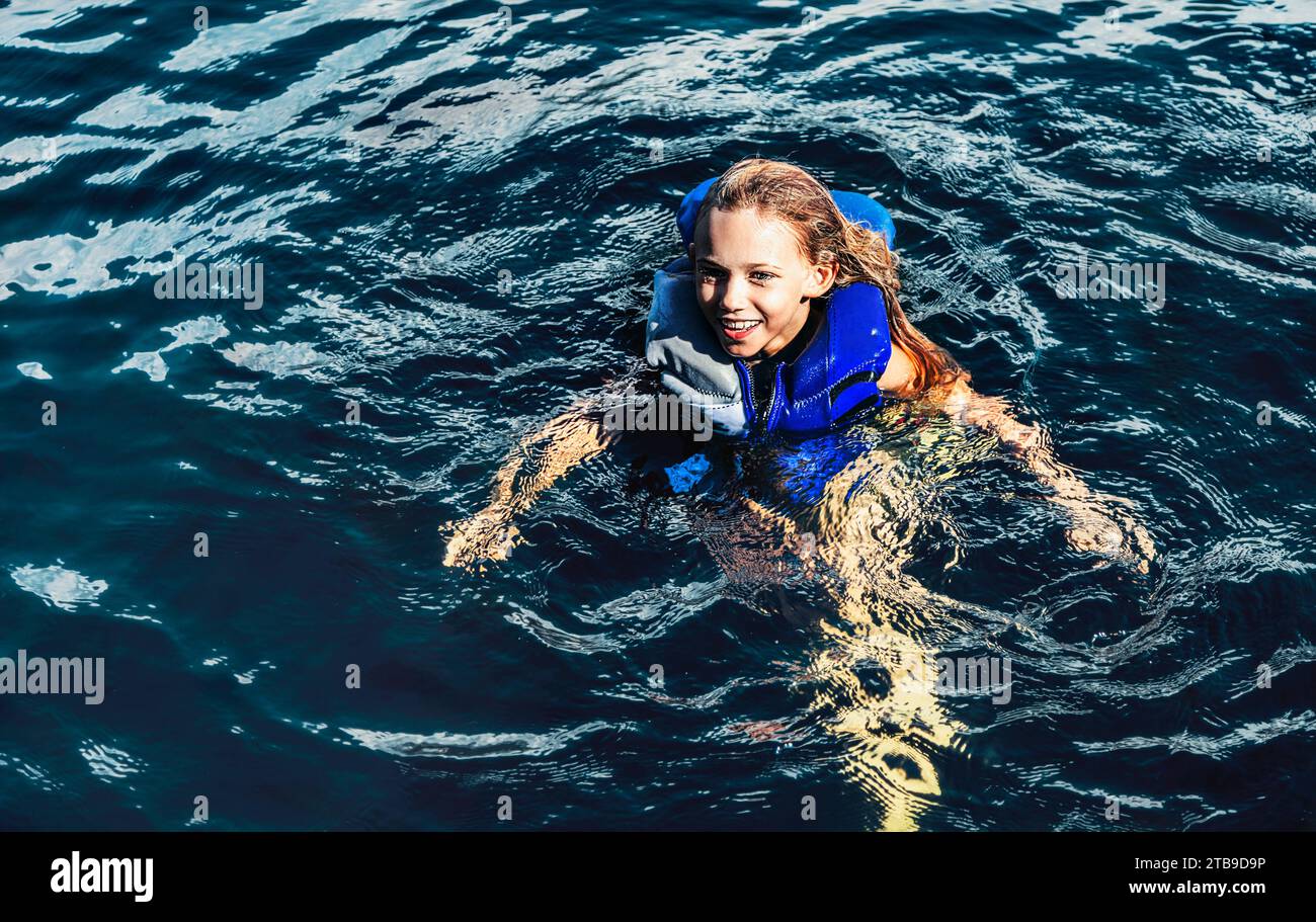 La giovane ragazza nuota in un lago limpido con un giubbotto di salvataggio blu, il lago Shuswap; British Columbia, Canada Foto Stock
