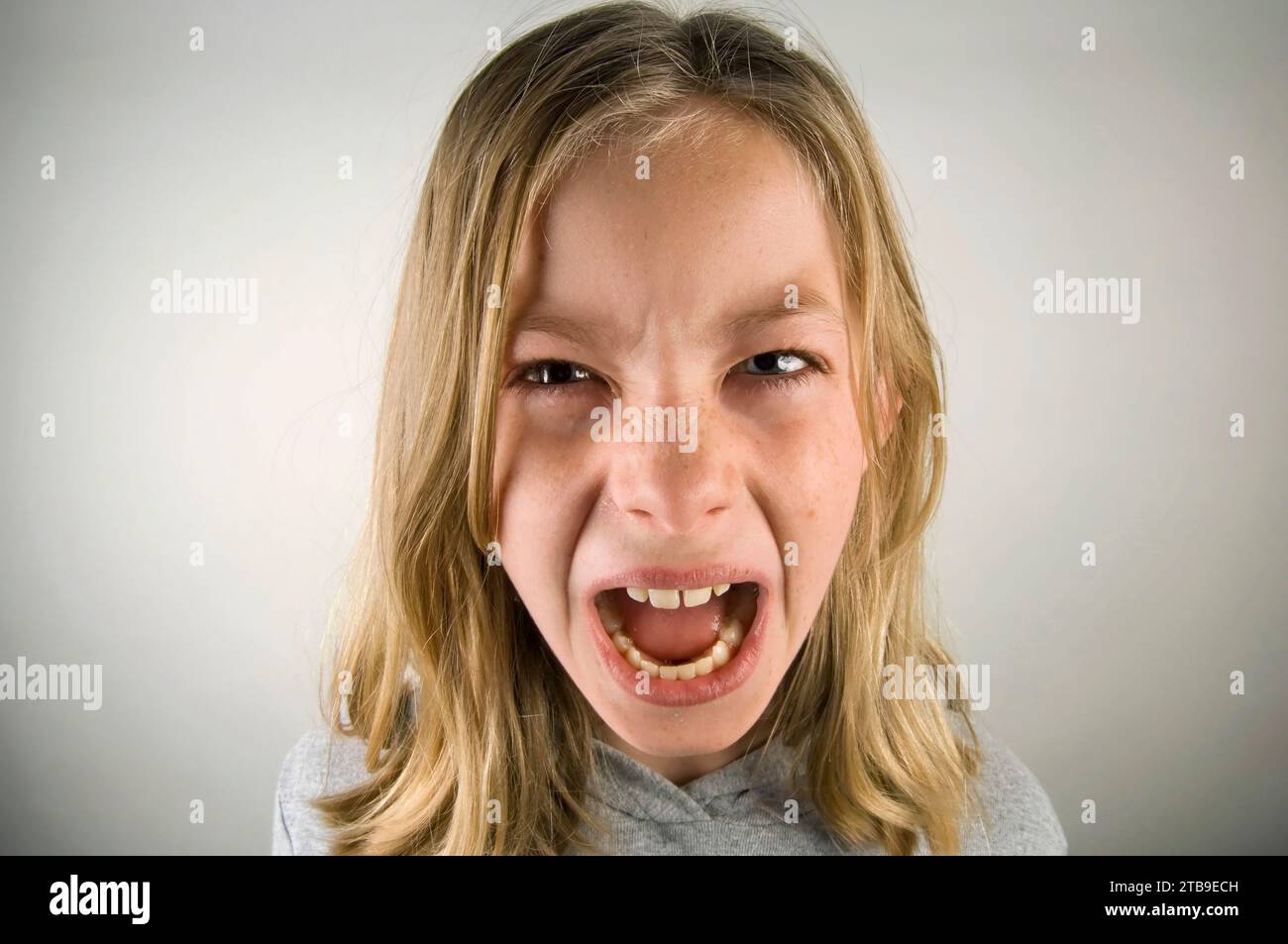 Preteen girl con un'espressione arrabbiata su sfondo grigio; Studio Foto Stock