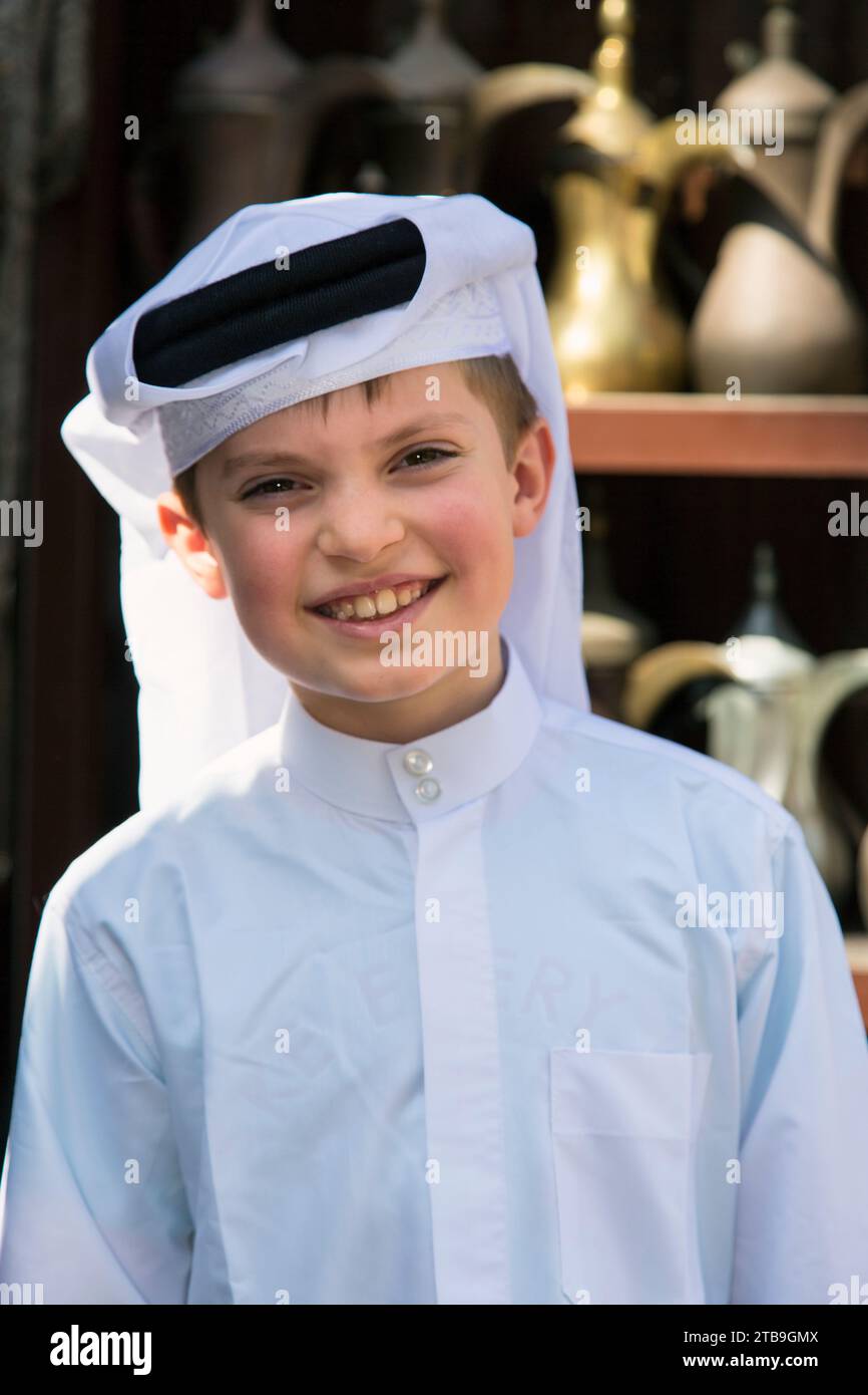 Ritratto ravvicinato di un giovane ragazzo arabo in abito tradizionale sorridente alla macchina fotografica al mercato Souq Waqif di Doha; Doha, Qatar Foto Stock