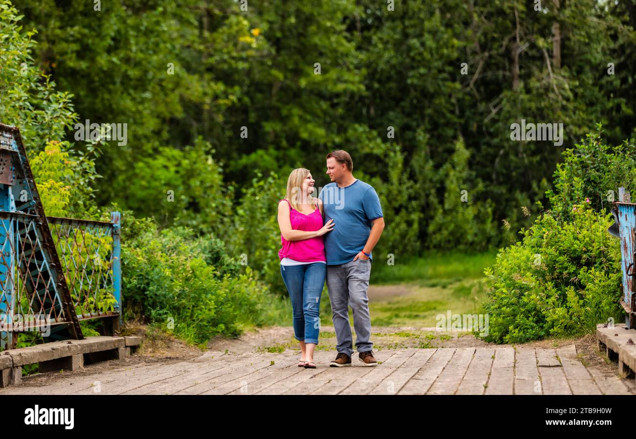 Ritratto di una coppia che cammina su un ponte a cavalletto di legno che abbraccia e si guarda mentre si fa una passeggiata nella natura in un parco Foto Stock