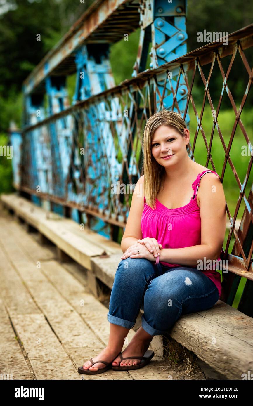 Ritratto ravvicinato di una donna seduta su una panchina di legno lungo un ponte a cavalletto durante una passeggiata nella natura in un parco, in posa per la macchina fotografica Foto Stock