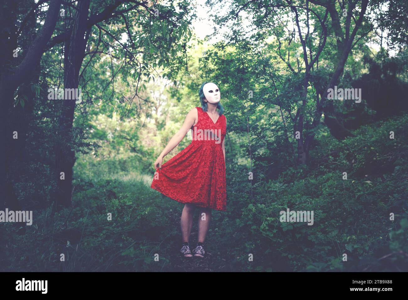 donna con maschera sul viso e abito rosso che balla in una foresta, concetto astratto Foto Stock