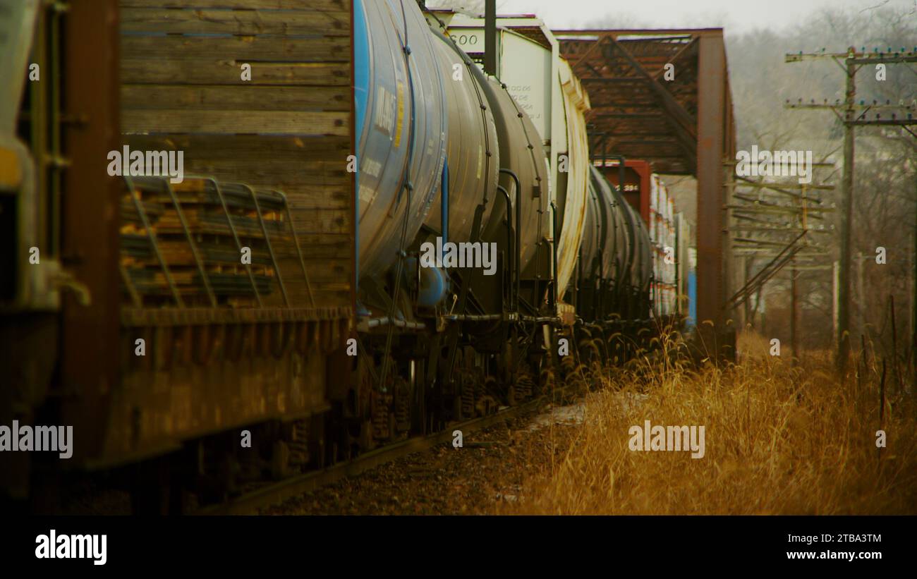 Un treno merci in movimento lento si avvicina e attraversa un ponte arrugginito in un paesaggio rustico e desolato del midwest Foto Stock