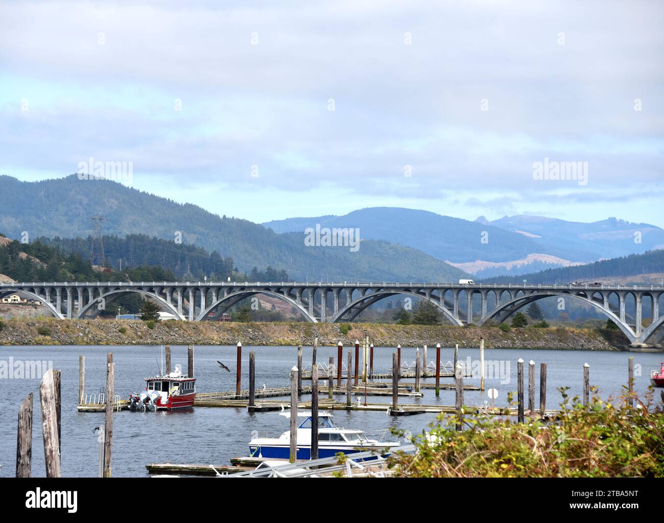 Il ponte Patterson attraversa il fiume Rogue a Gold Beach, Oregon. Il design Art Deco presenta diversi archi in cemento. Barche ancorate in primo piano. Foto Stock