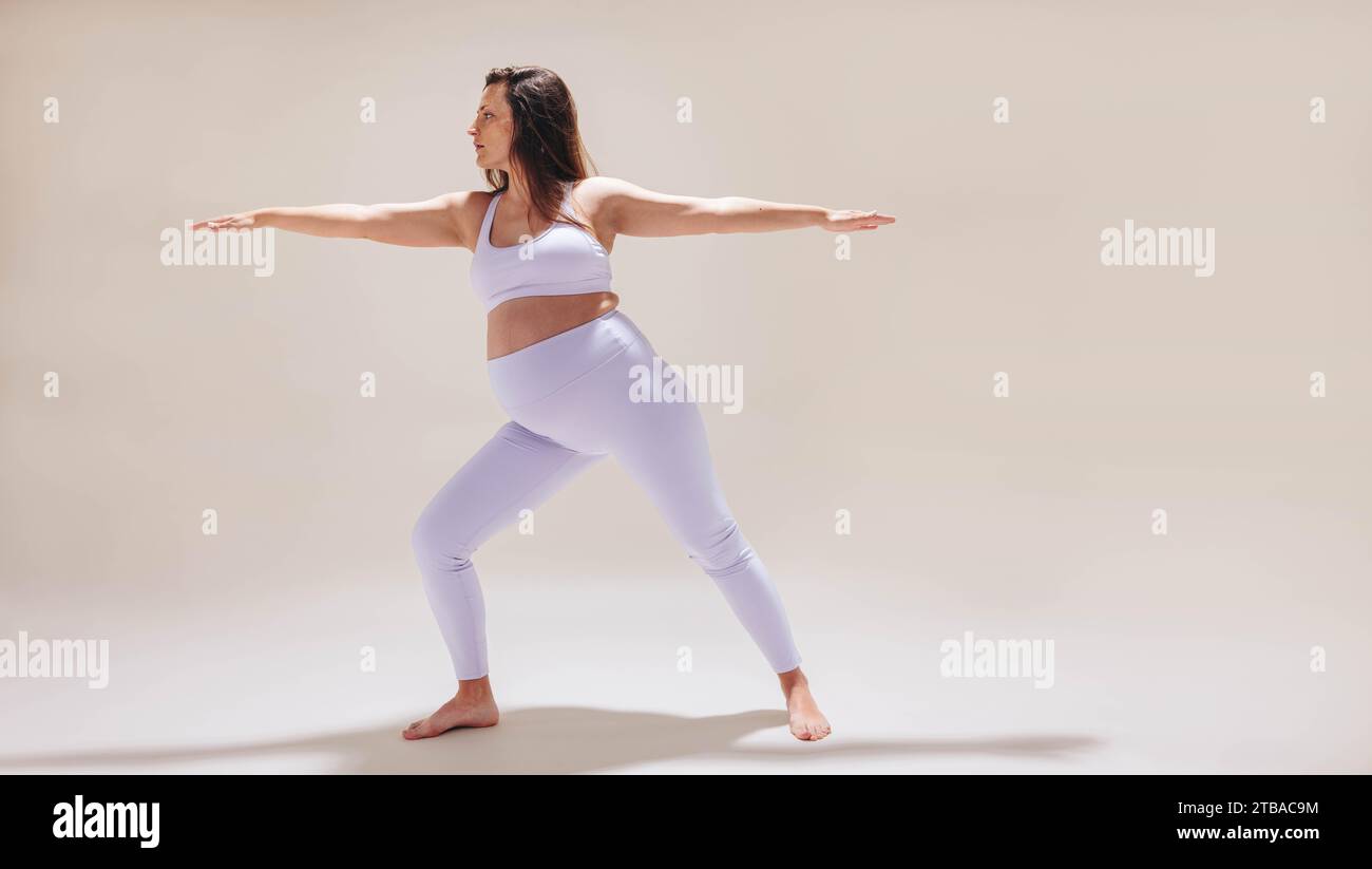In uno studio, una donna incinta nel suo terzo trimestre pratica yoga prenatale. Impegnandosi nello stretching dolce e nell'esercizio fisico, enfatizza il suo corpo Foto Stock