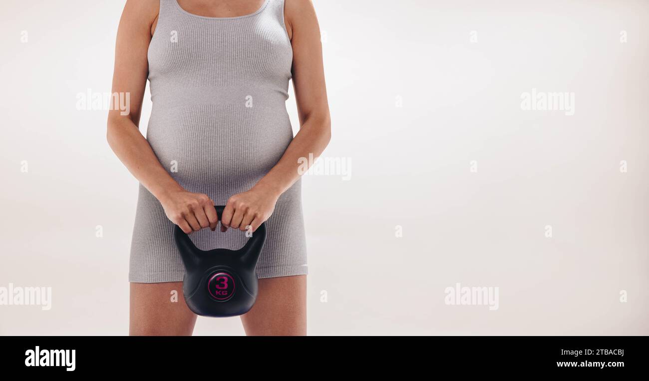 donna incinta che fa esercizio in uno studio, promuovendo la salute e il benessere del nascituro. Donna che indossa abbigliamento fitness, sollevamento pesi e focu Foto Stock