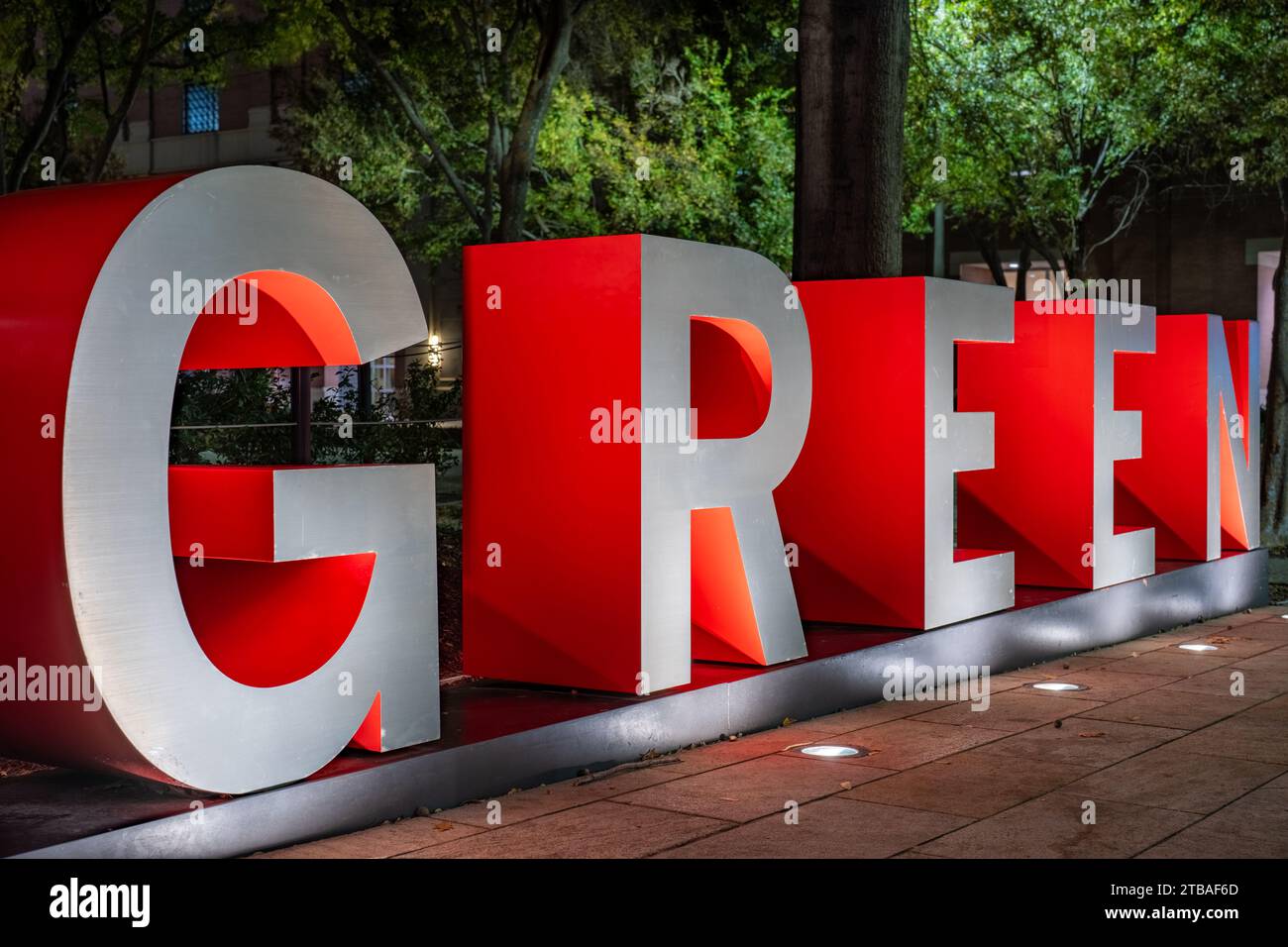 Le lettere 3d tridimensionali rosse e grigie formano la parola VERDE con uno sfondo serale all'aperto. Foto Stock