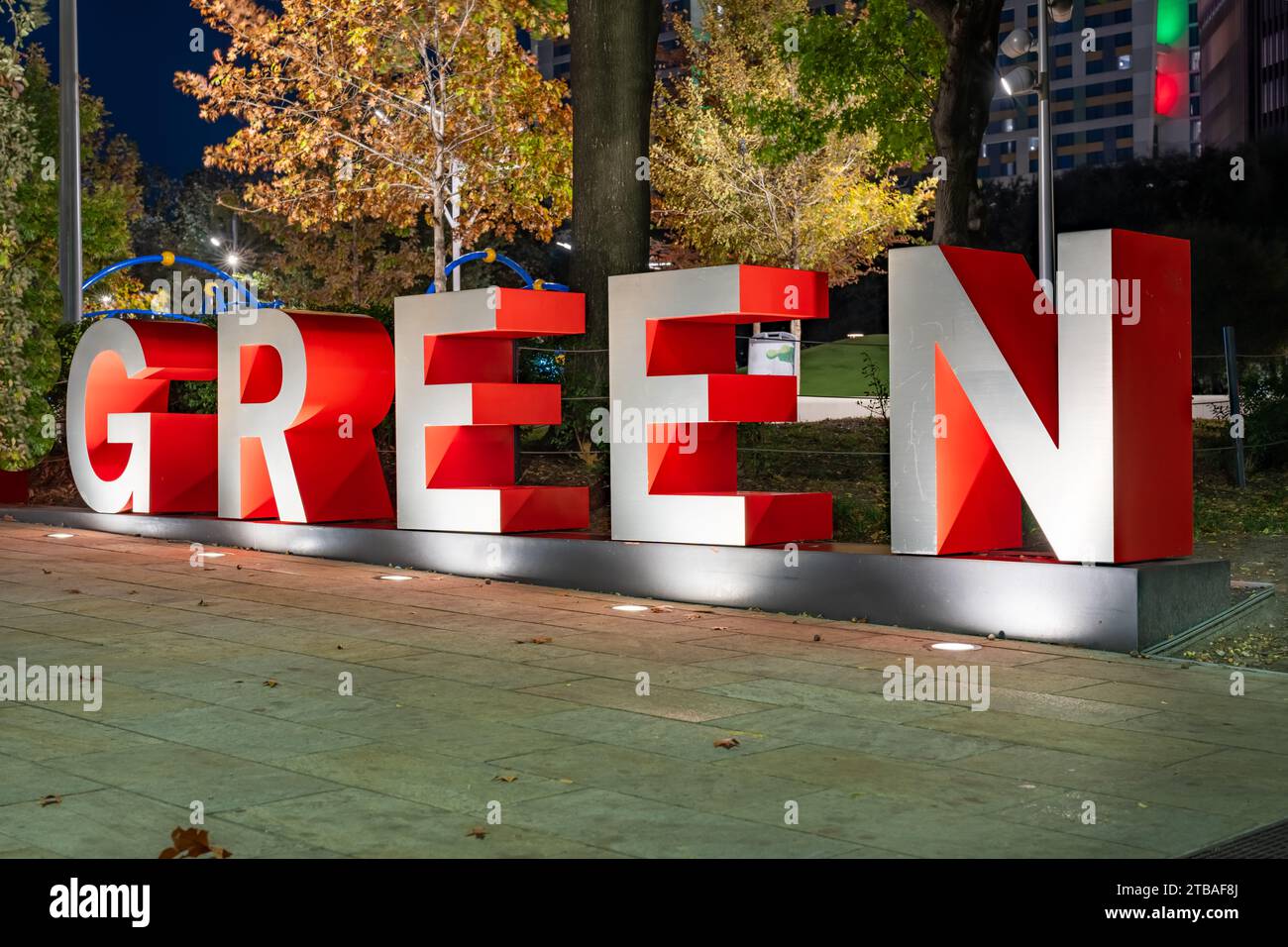 Le lettere 3d tridimensionali rosse e grigie formano la parola VERDE con uno sfondo serale all'aperto. Foto Stock