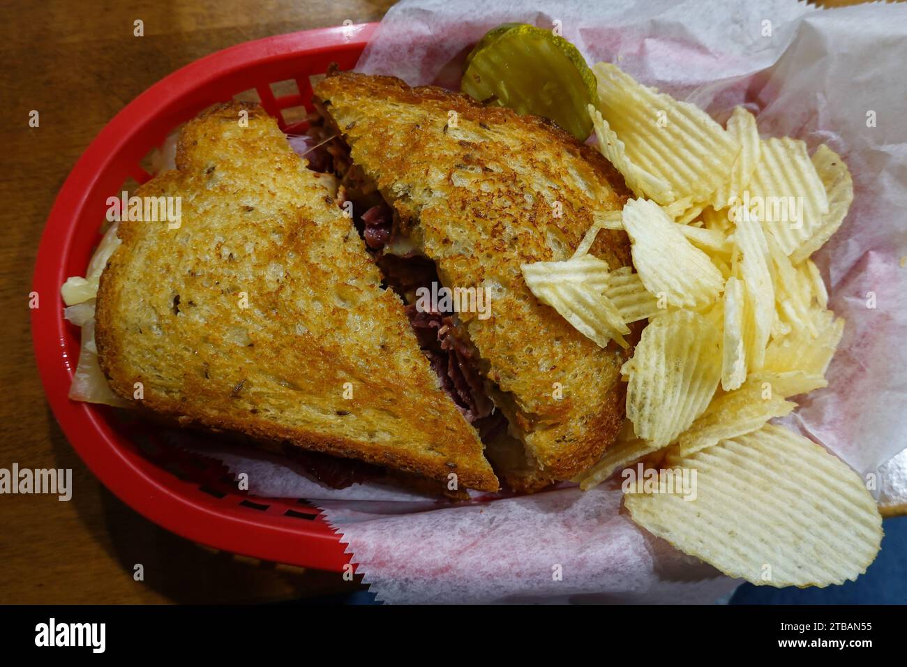 Un classico sandwich Reuben servito in un cestino con patatine fritte e sottaceti a base di carne in scatola, crauti, formaggio svizzero e salsa speciale. Foto Stock