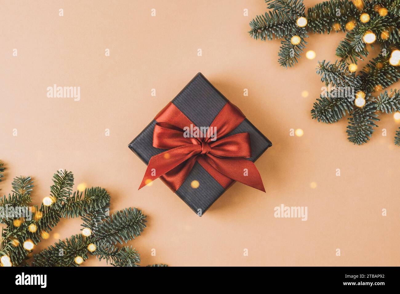 Confezione regalo con fiocco rosso e rami di abete su sfondo beige. Vista dall'alto, base piatta. Foto Stock