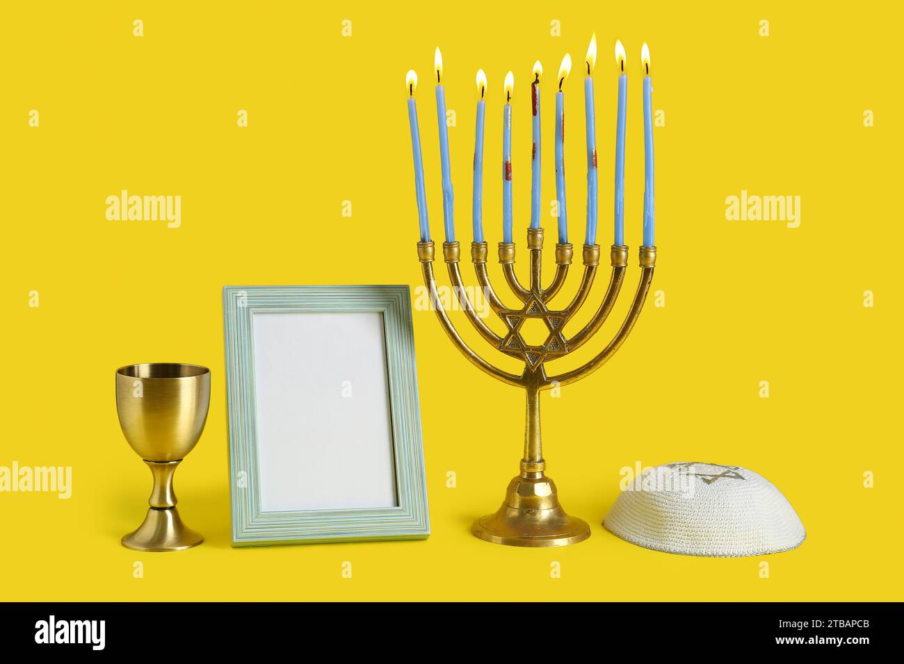 Menorah, kippah, cornice vuota e tazza per la celebrazione Hanukkah su sfondo giallo Foto Stock