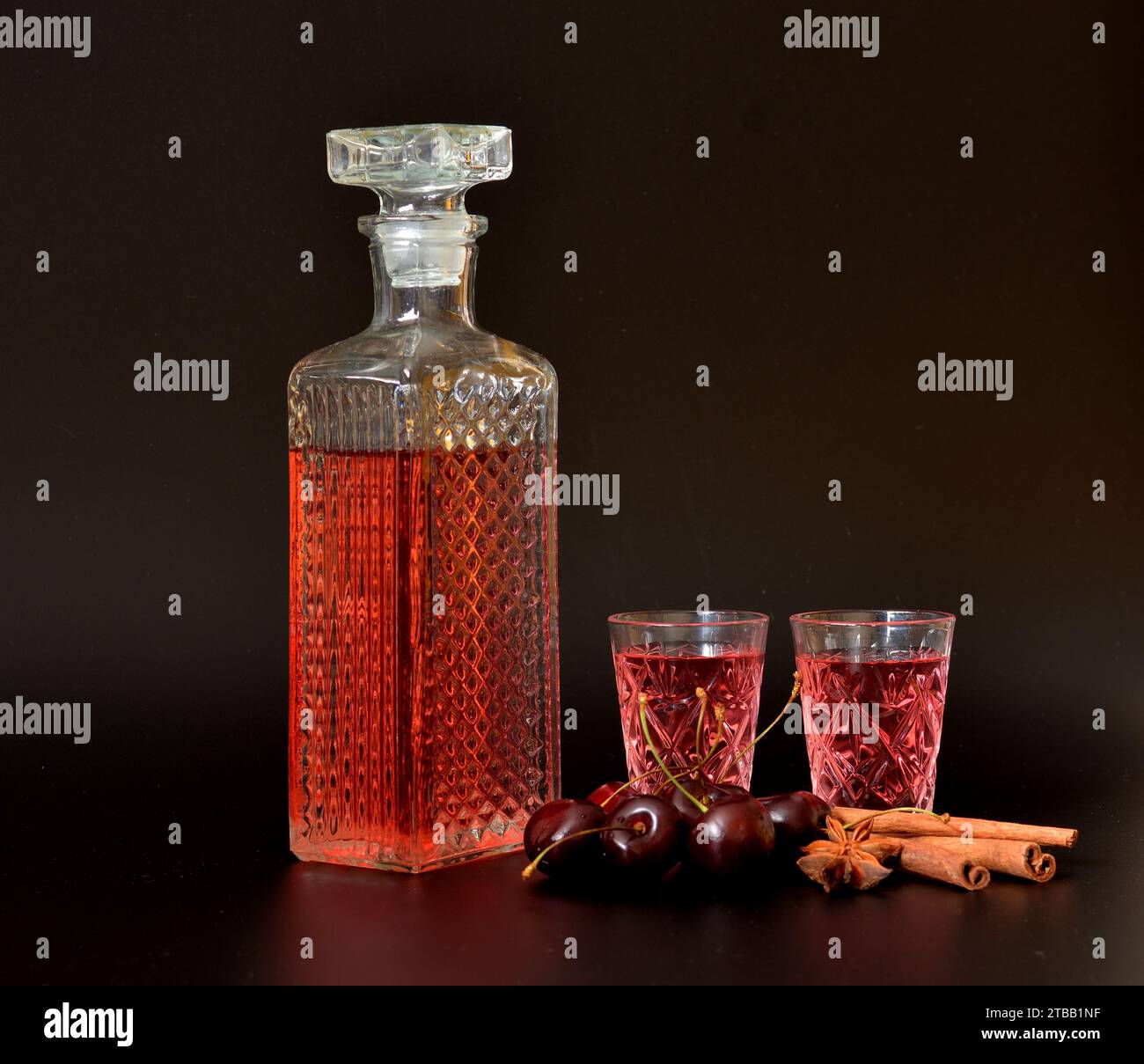 Liquore alla ciliegia con spezie, forte alcol fatto in casa in un decanter di cristallo e due bicchieri su sfondo nero, accanto a bastoncini di anice e cannella. CL Foto Stock
