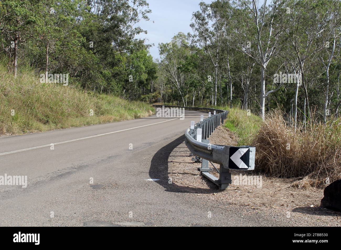 Hervey Range Road, circondata da alberi ed erba, con una barriera di guardia nel Queensland settentrionale, Australia Foto Stock