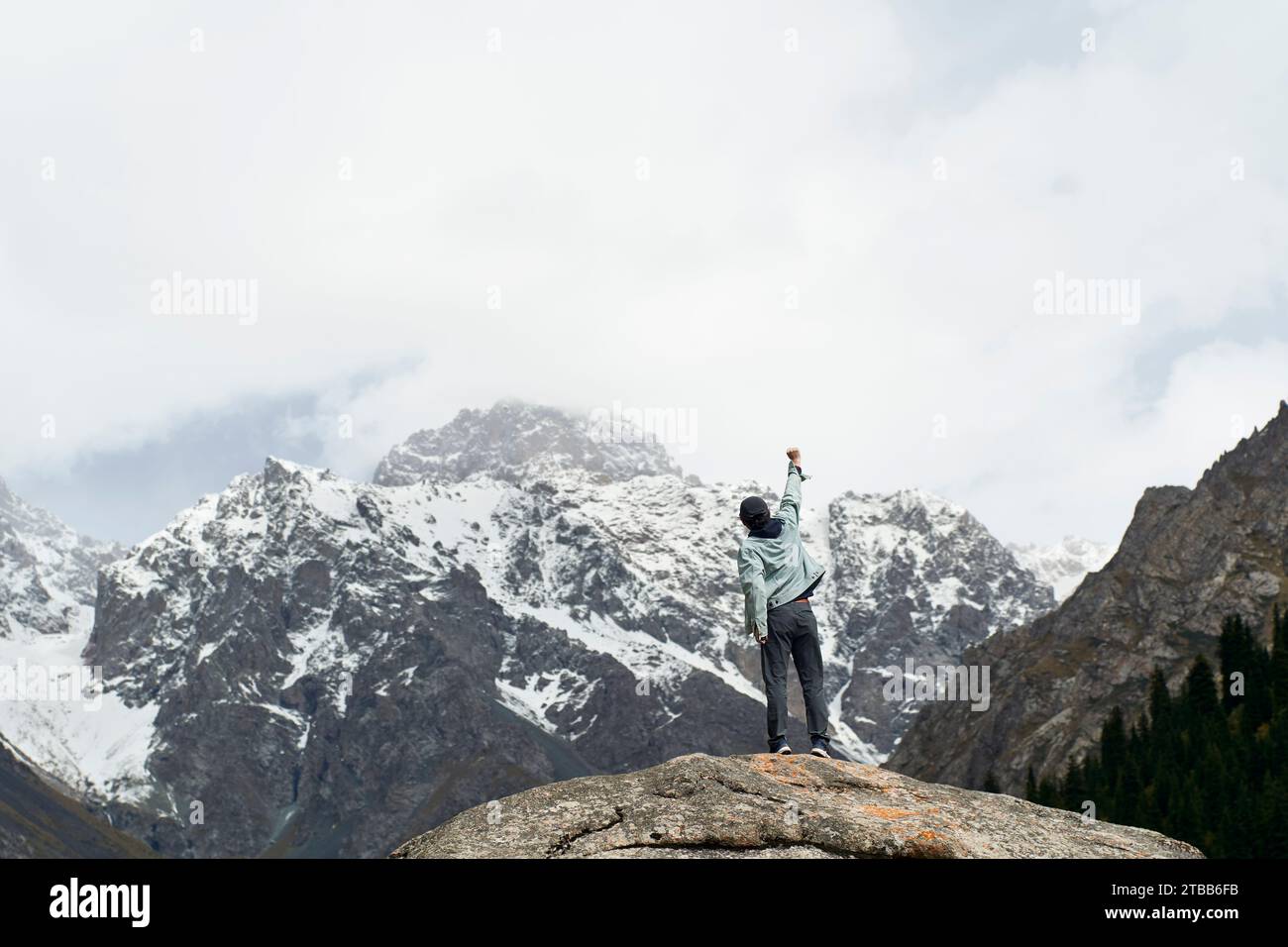 Vista posteriore di un viaggiatore asiatico in cima a una roccia che guarda una montagna di neve nello Xinjiang, Cina Foto Stock
