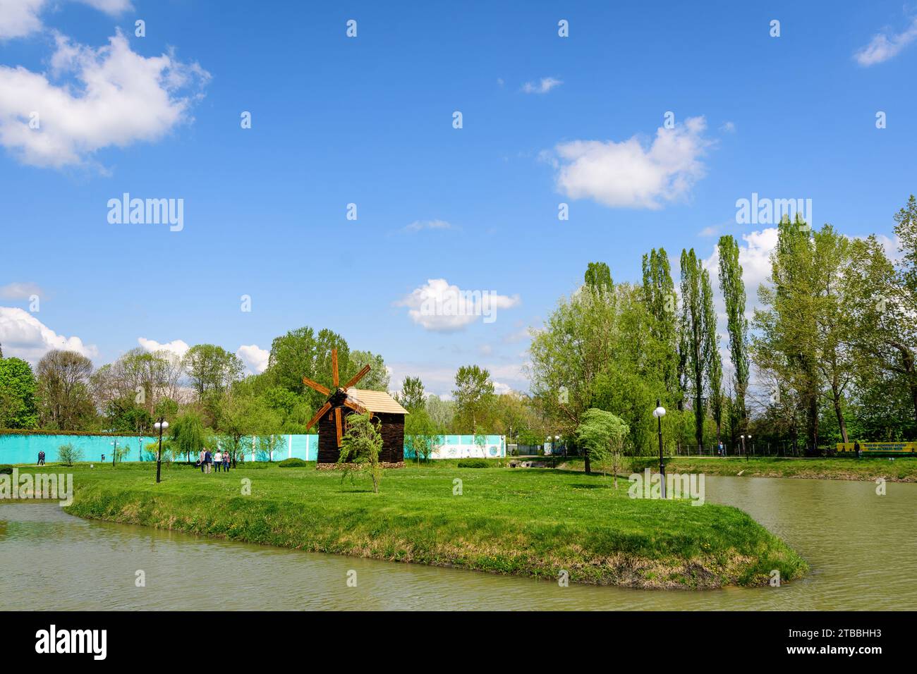 Piccolo lago con un mulino a legna e un'isola dal Parco Chindiei (Parcul Chindiei) a Targoviste, Romania, in una soleggiata giornata primaverile con nuvole bianche e blu Foto Stock