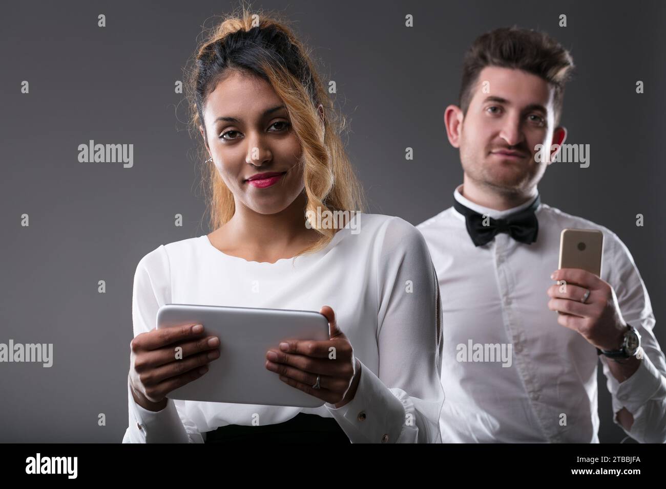 Una giovane donna nera ha un tablet, un uomo bianco con il telefono sullo sfondo Foto Stock