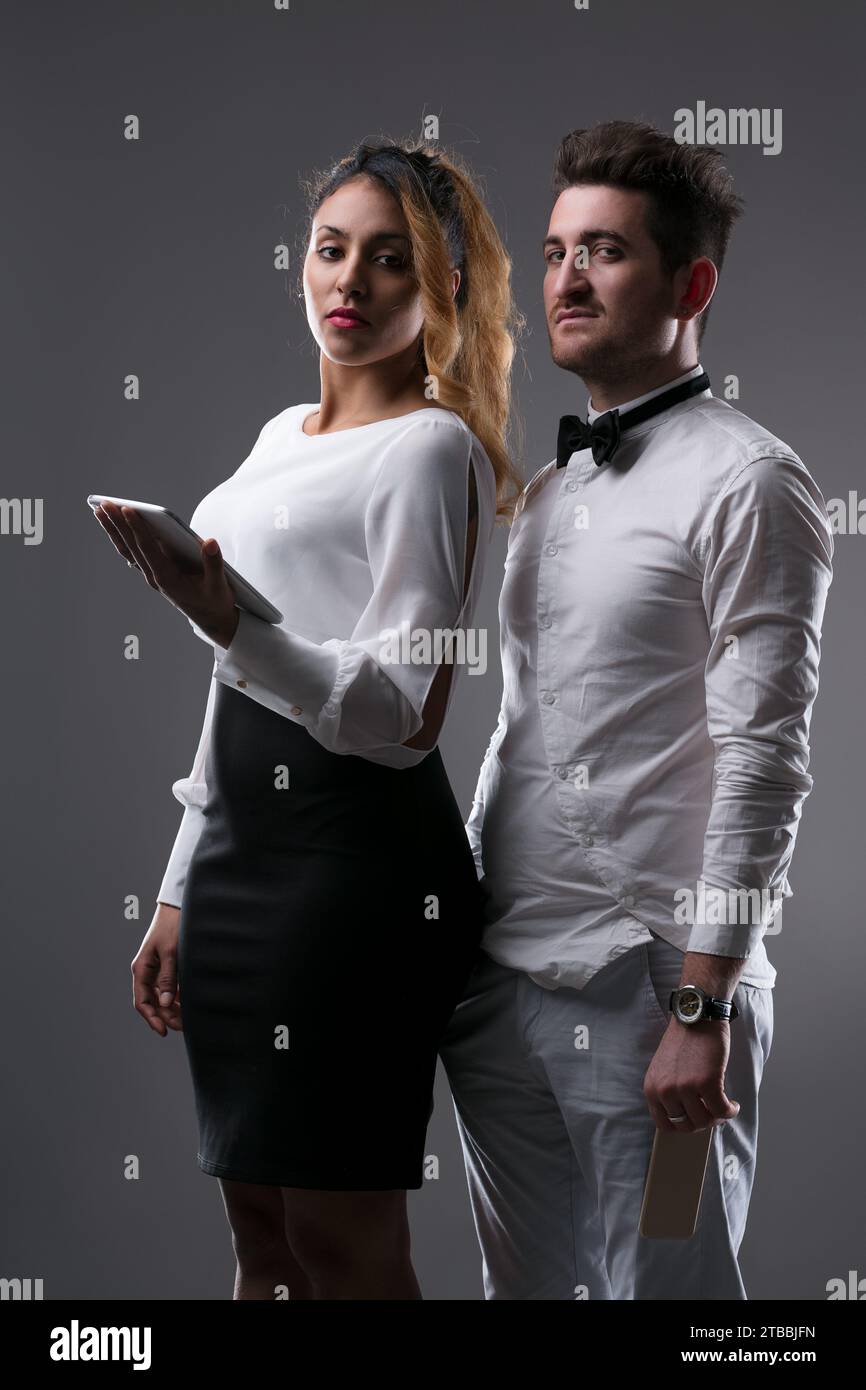 Coppia professionale impegnata con la tecnologia, lei con il tablet, lui con lo smartphone Foto Stock