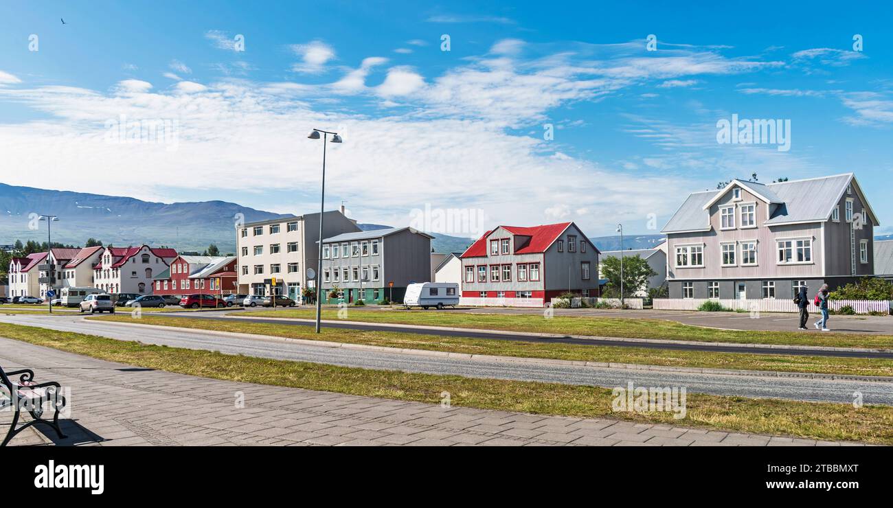 Ampia passerella su una piacevole strada fiancheggiata da piccoli appartamenti ad Akureyri in Islanda sotto un cielo estivo parzialmente nuvoloso Foto Stock