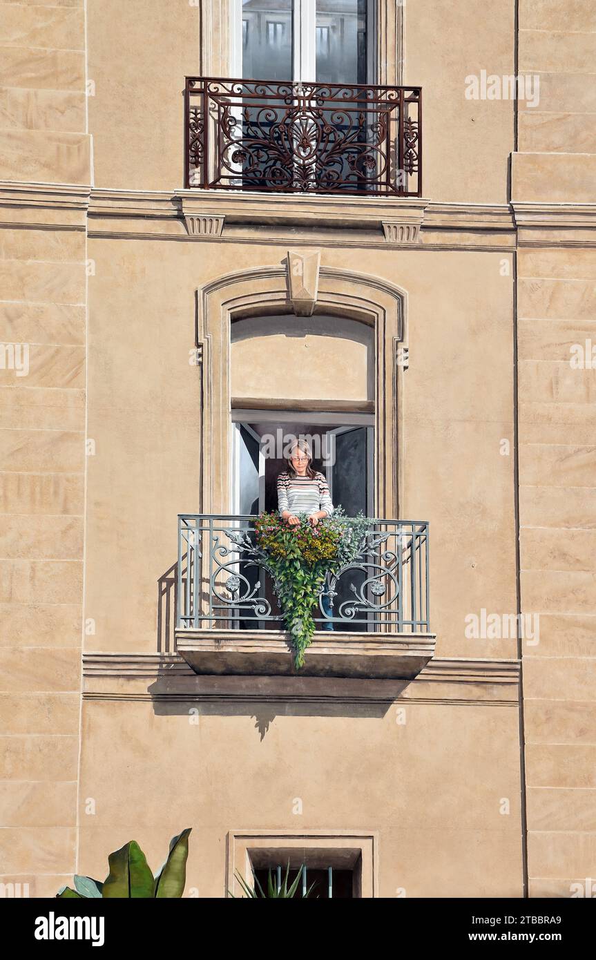 Tromp l'Oeil, finestre e balconi dipinti su una parete altrimenti completamente vuota, con una giovane signora che potava fiori sul balcone inferiore Foto Stock