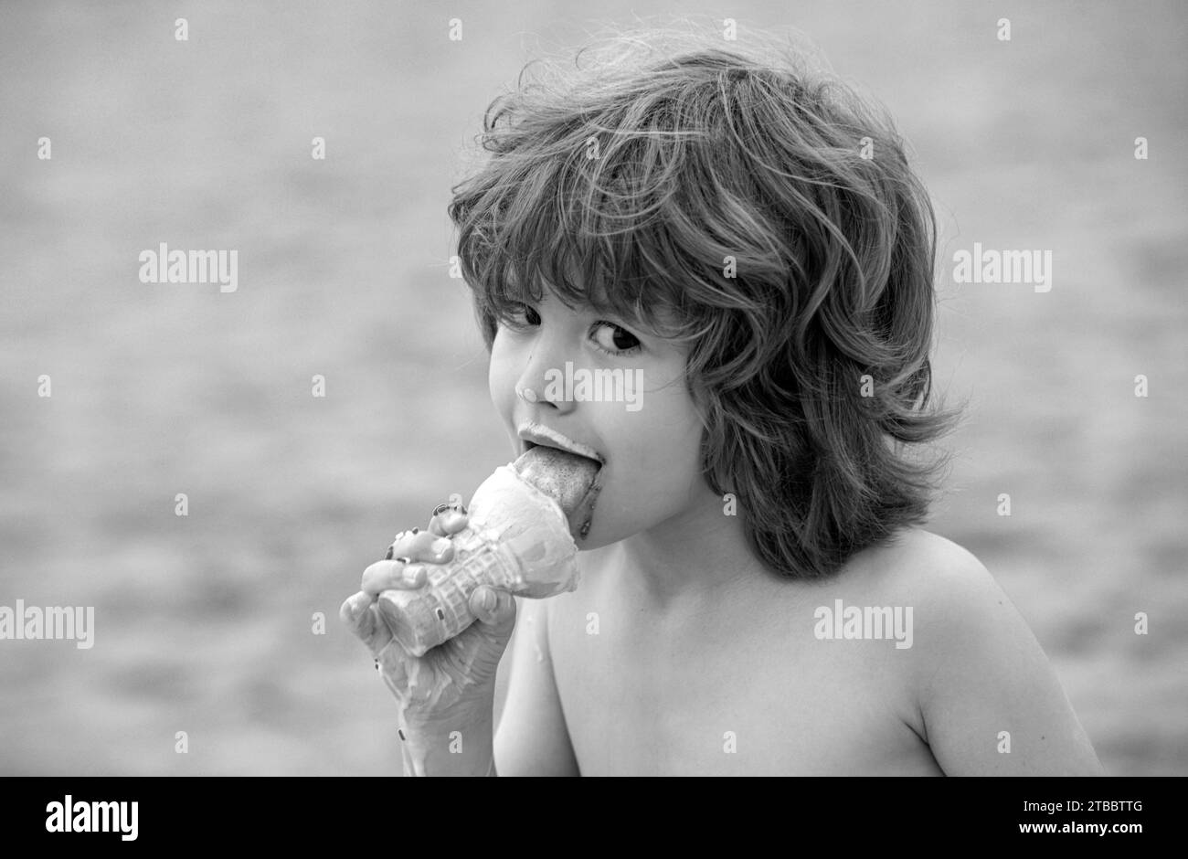 Un ragazzo carino che lecca un grande gelato nel cono dei waffle. Bambino che mangia gelato. Il ragazzo con la faccia sporca mangia il gelato Foto Stock