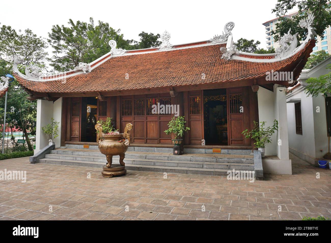Vista esterna di un tempio buddista con tetto a pagoda in piastrelle di argilla con sculture bianche di drago sulle creste. Davanti si trova un'ampia urna di incenso in bronzo Foto Stock