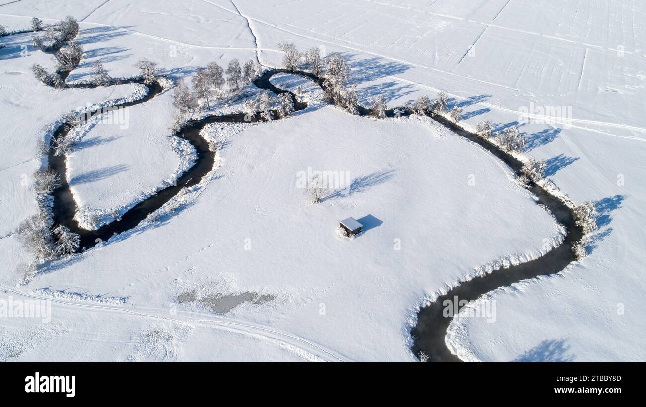 Colpo di drone del fiume Schmutter che si snoda naturalmente attraverso il paesaggio innevato e incontaminato del parco naturale Westeliche Wälder vicino ad Augusta, Svevia, Foto Stock