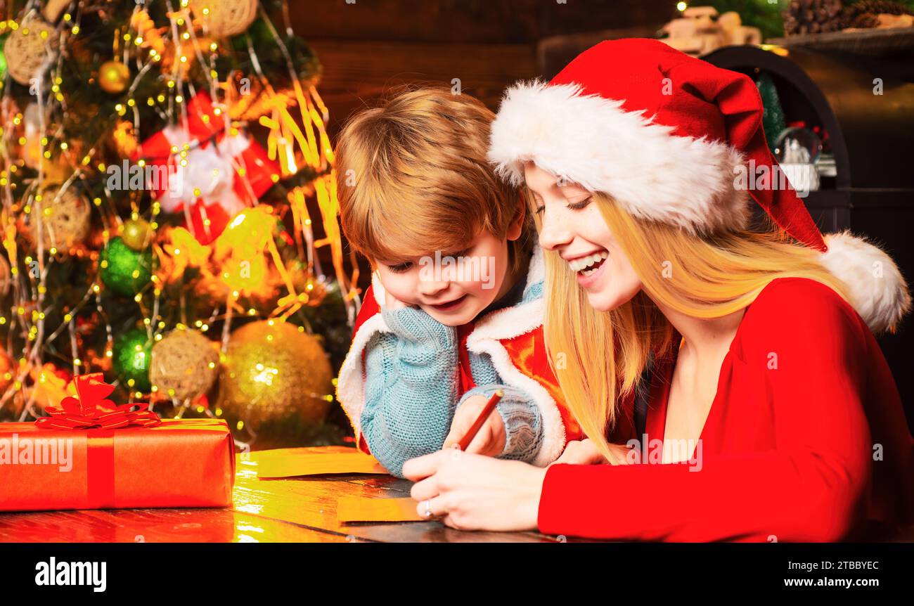 Mamma e ragazzo scrivono la lista dei desideri a santa.play insieme, la vigilia di natale. Madre e bambino che si divertono. Famiglia che si diverte a casa albero di natale. Foto Stock