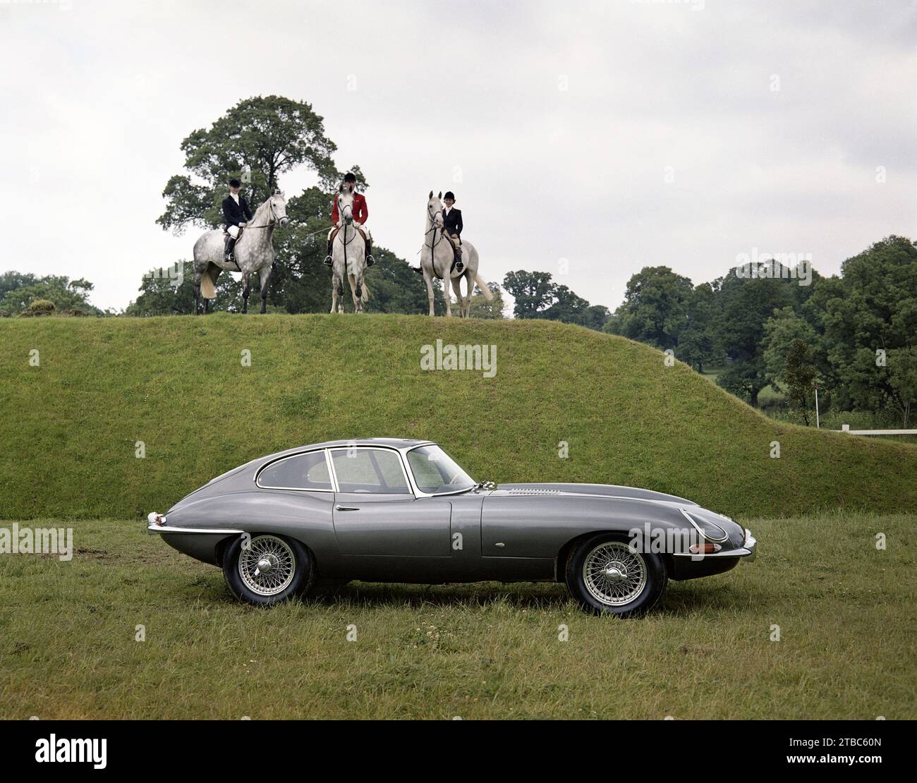 1961 Jaguar e-TYPE serie 1 Coupé a testa fissa, 9600 CV, trascurata da tre cavalli e cavalieri sul Derby Bank, durante le prove di Hickstead Horse Foto Stock