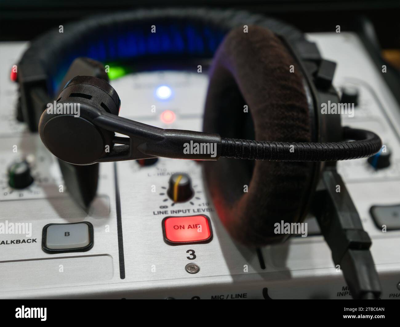 Primo piano di una console di missaggio con pulsante luminoso sull'aria e cuffia sul posto di lavoro di un commentatore sportivo Foto Stock