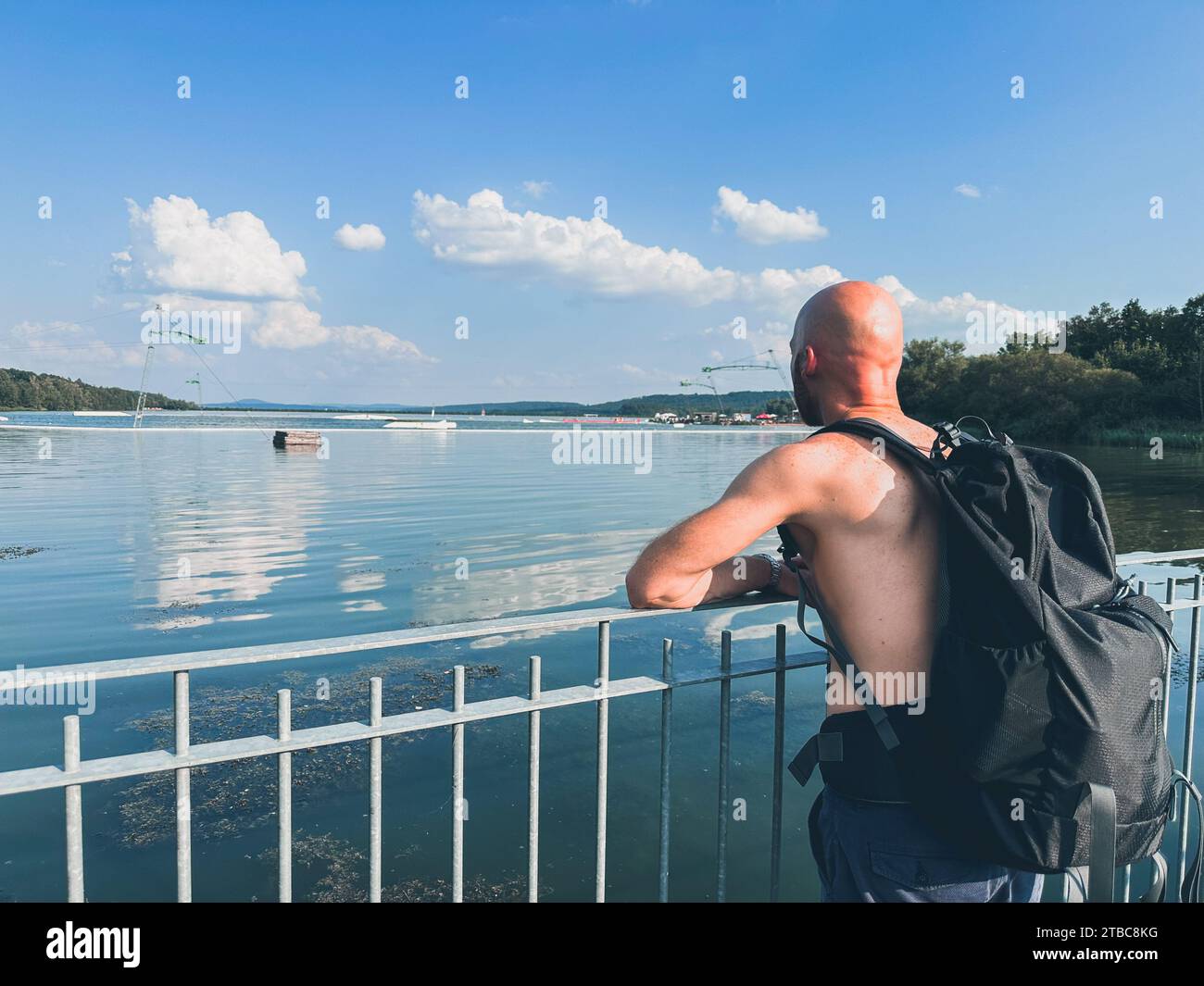 Un uomo senza vestiti in cima che guarda lontano da un ponte in una giornata un po' nuvolosa ma soleggiata con un cielo blu Foto Stock