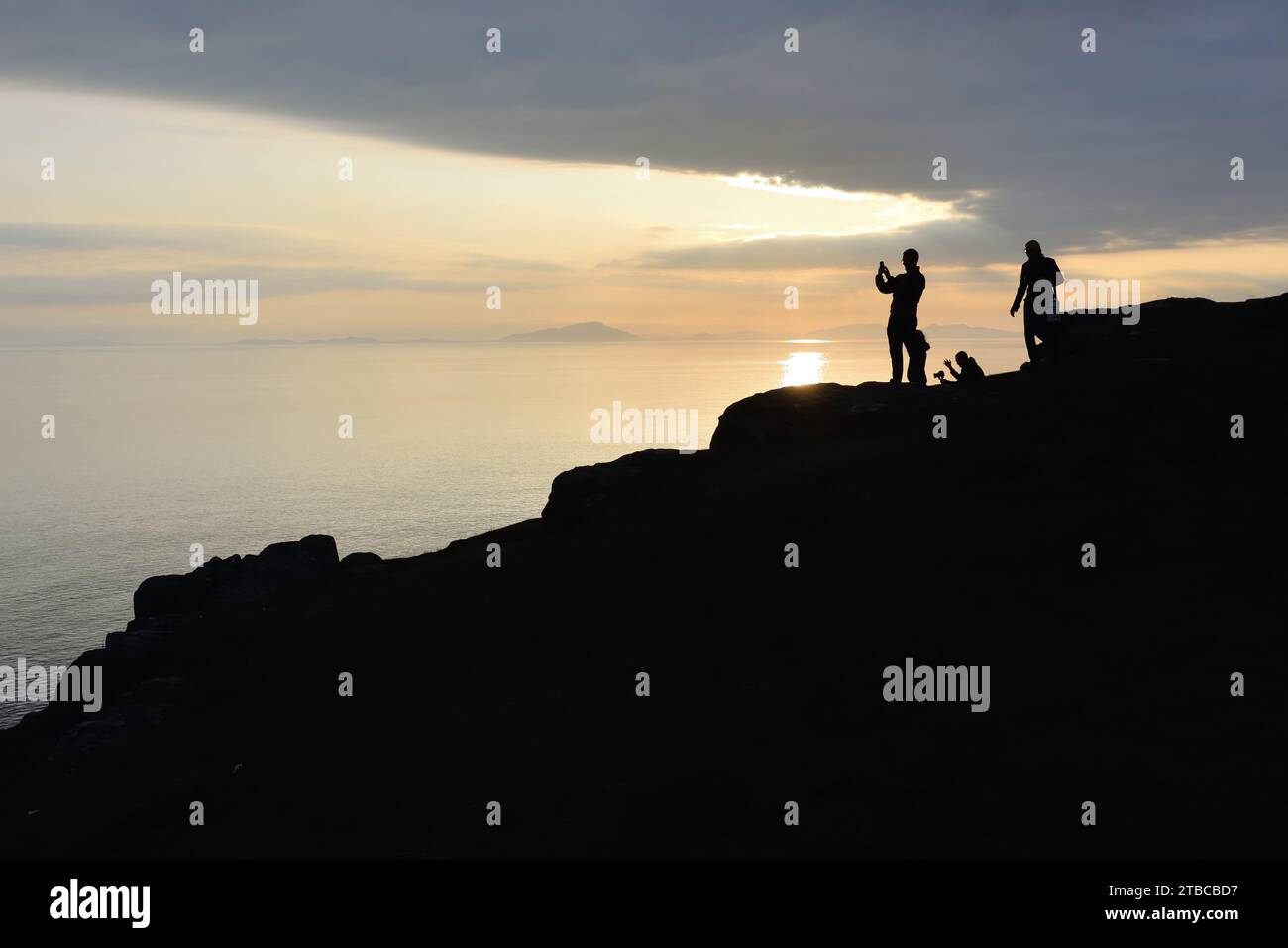 Un gruppo di turisti che scattano foto di un tramonto sull'Atlantico a Neist Point sull'isola di Skye, in Scozia. Foto Stock