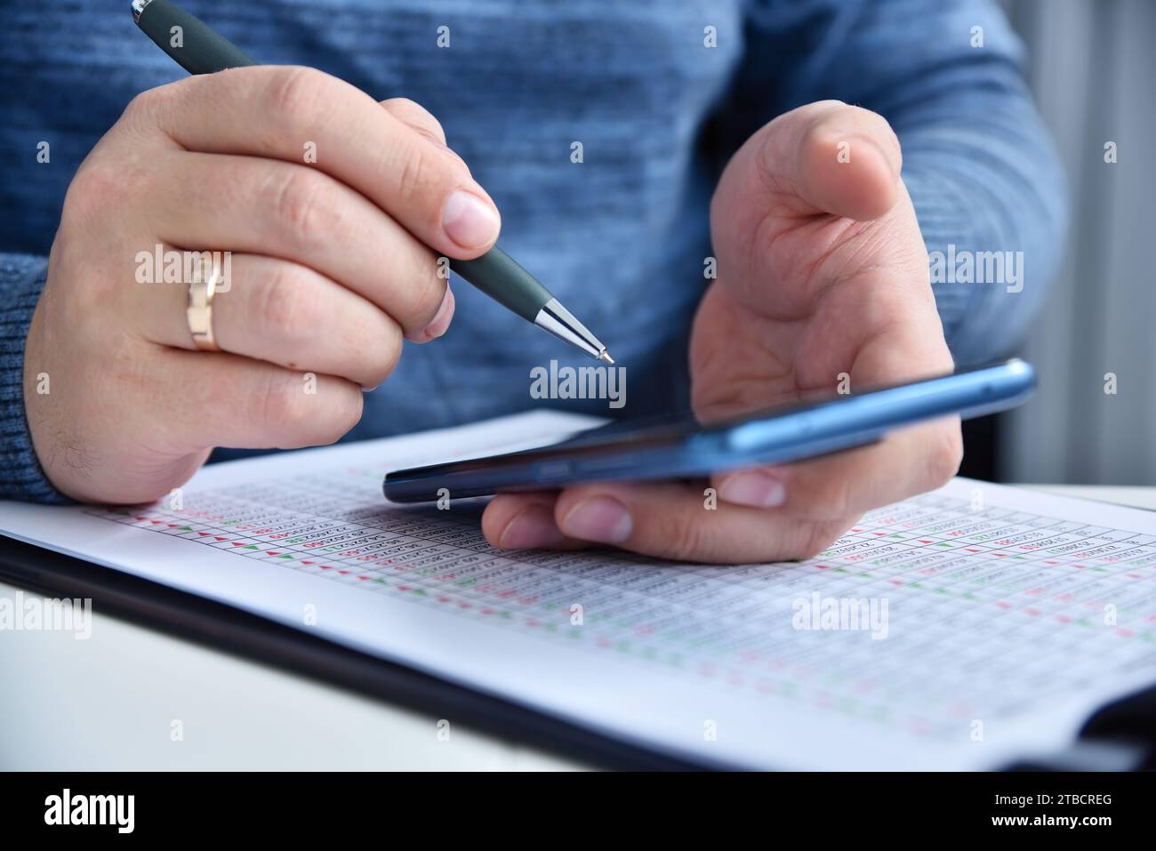 Le mani di un uomo d'affari reggono il telefono di mobiló. Relazione finanziaria sul tavolo. Concetto economico e finanziario. Primo piano Foto Stock
