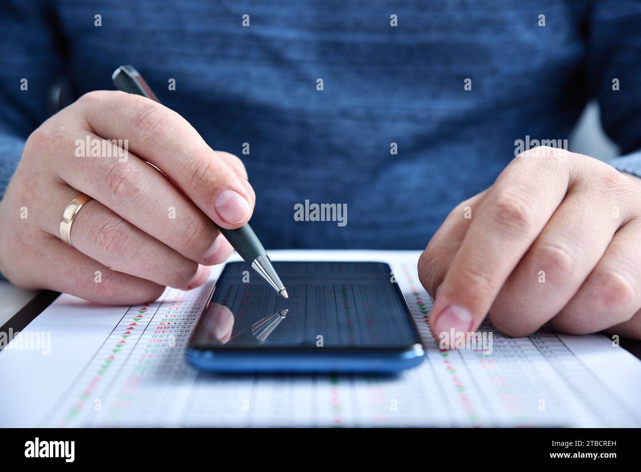 Busiessman con penna in mano utilizzando il telefono cellulare con statistiche di magazzino sullo schermo. Business concept e trading su Internet. Primo piano Foto Stock