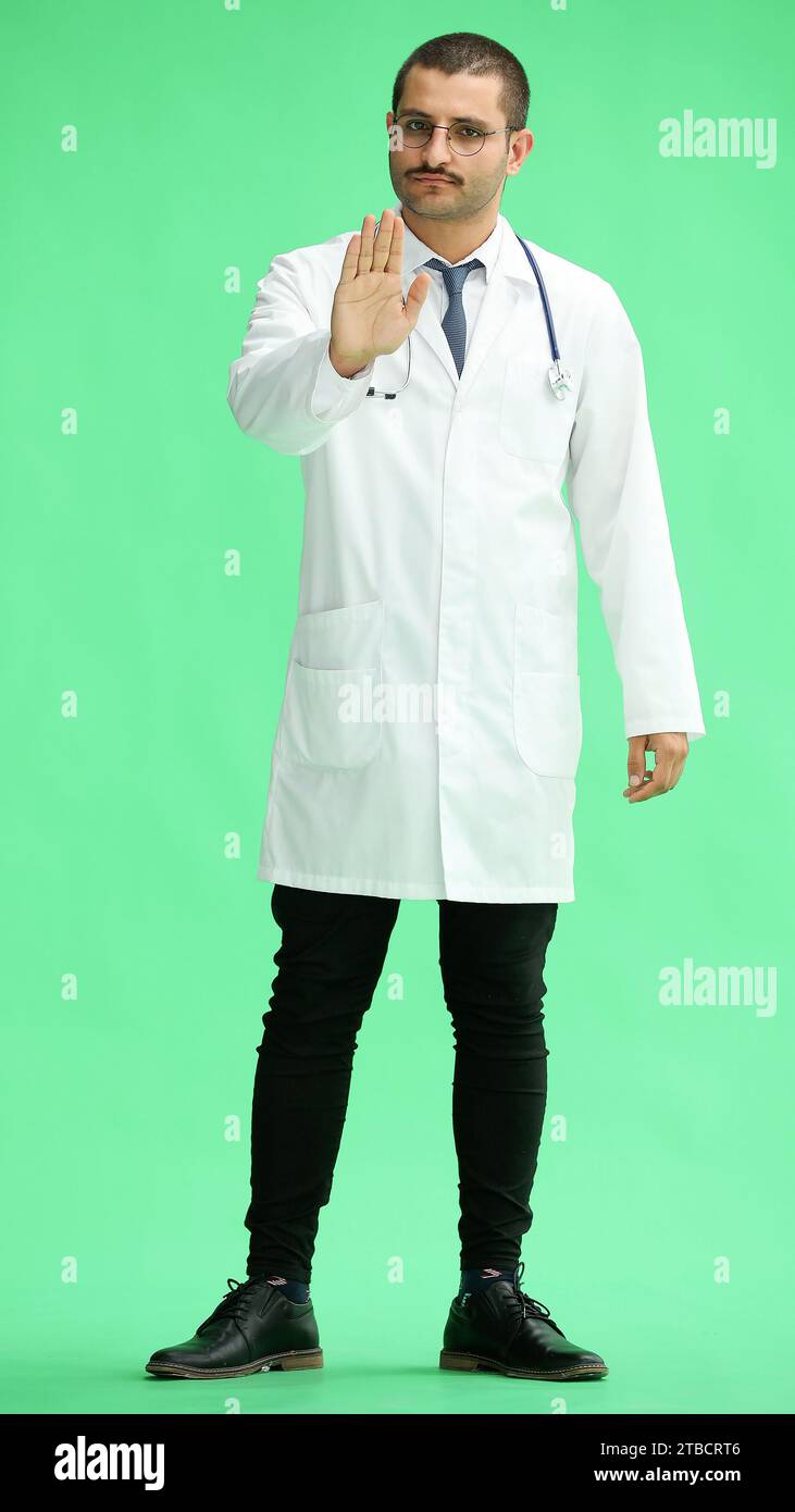 un medico di sesso maschile con un mantello bianco su sfondo verde mostra un segnale di stop Foto Stock