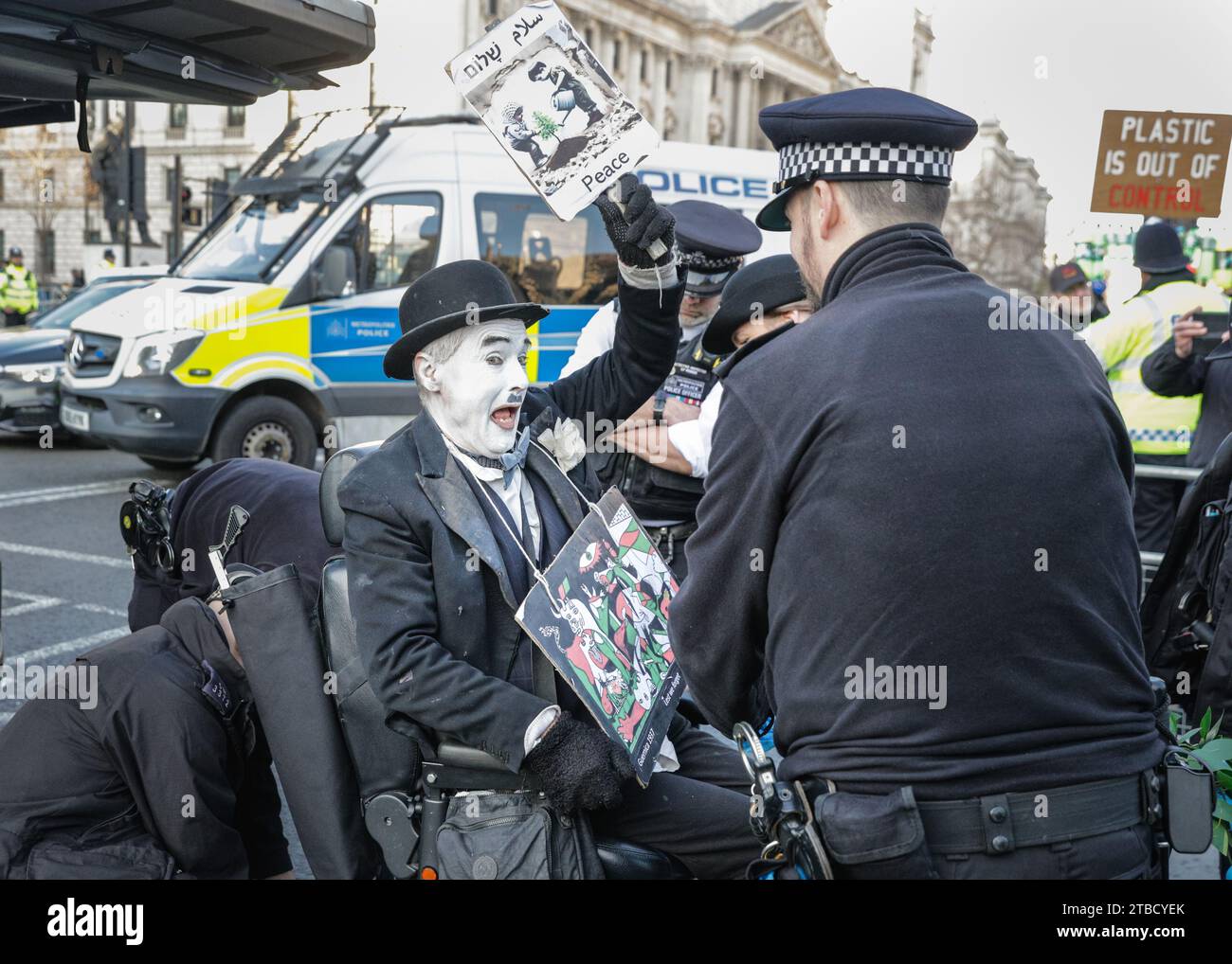 Londra, Regno Unito. 6 dicembre 2023. Il manifestante viene arrestato. Un manifestante vestito da Charles Chaplin, che trasmette un messaggio di "pace" riguardo al conflitto israelo-Hamas, sta bloccando i cancelli d'ingresso principali delle camere del Parlamento di Westminster con il suo scooter di mobilità. Il manifestante ha problemi di linguaggio e mobilità, e sembra pacifico, ma si rifiuta di muoversi dai cancelli e alla fine viene arrestato e scrupolosamente spostato in un veicolo speciale della polizia con una rampa. Crediti: Imageplotter/Alamy Live News Foto Stock