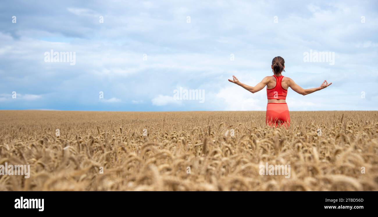 Vista posteriore di una donna che medita in un campo di grano. Allontanarsi da tutto. Foto Stock