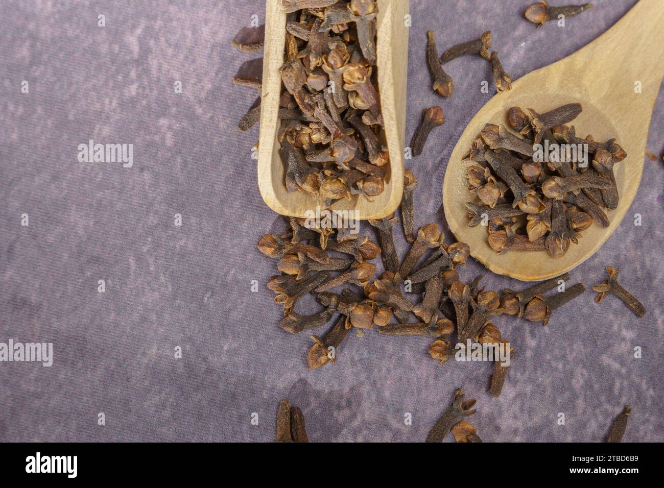 Asciugare i semi di chiodi di garofano in un cucchiaio di legno a fuoco selettivo e su uno sfondo di panno viola Foto Stock