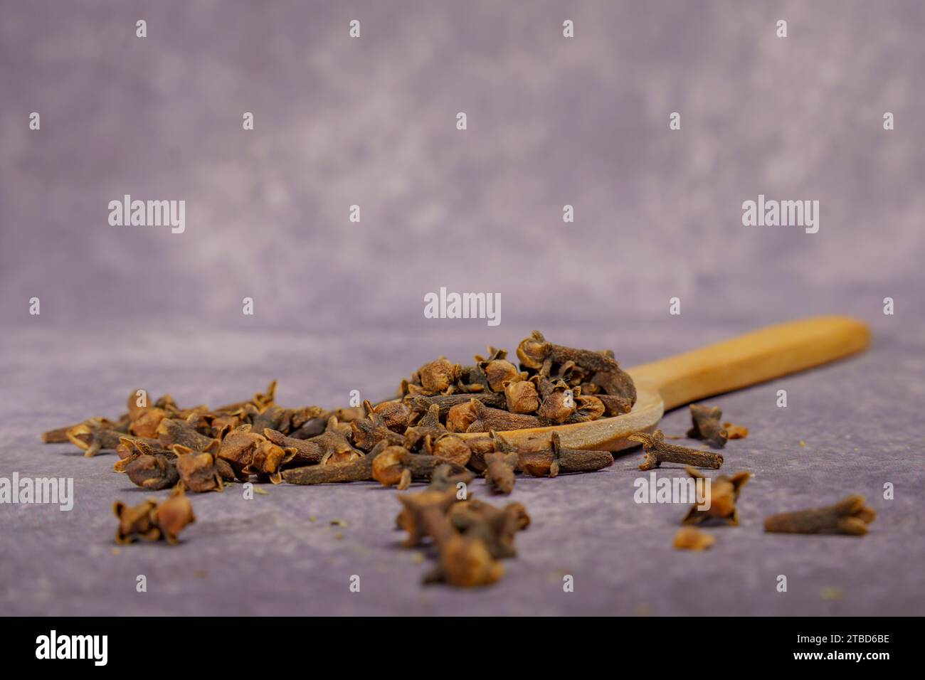 Asciugare i semi di chiodi di garofano in un cucchiaio di legno a fuoco selettivo e su uno sfondo di panno viola Foto Stock