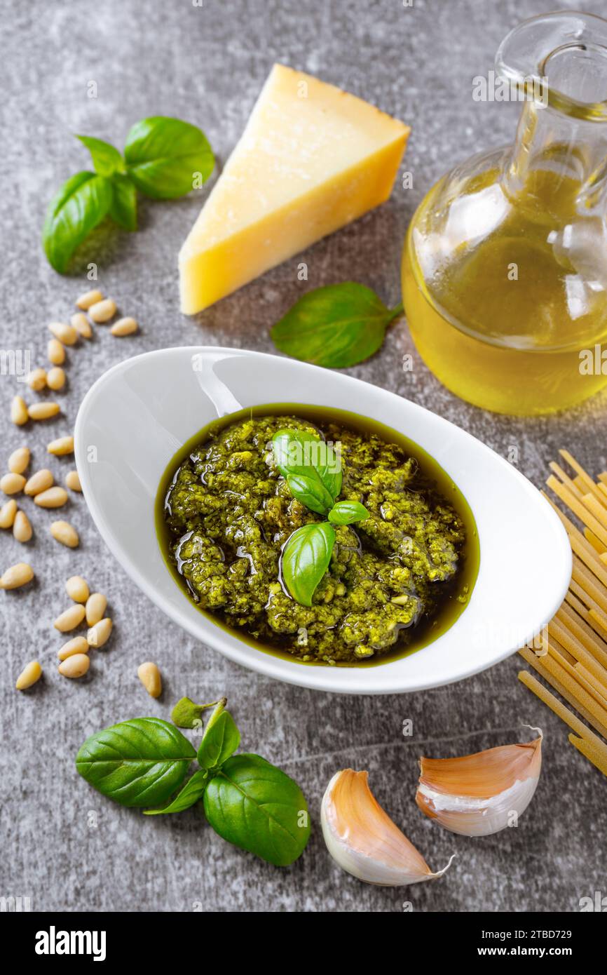 Pesto fatto in casa in piccolo vaso di vetro e ingredienti per la pasta su cemento grigio. Cucina tradizionale italiana, ricette, menu del ristorante Foto Stock