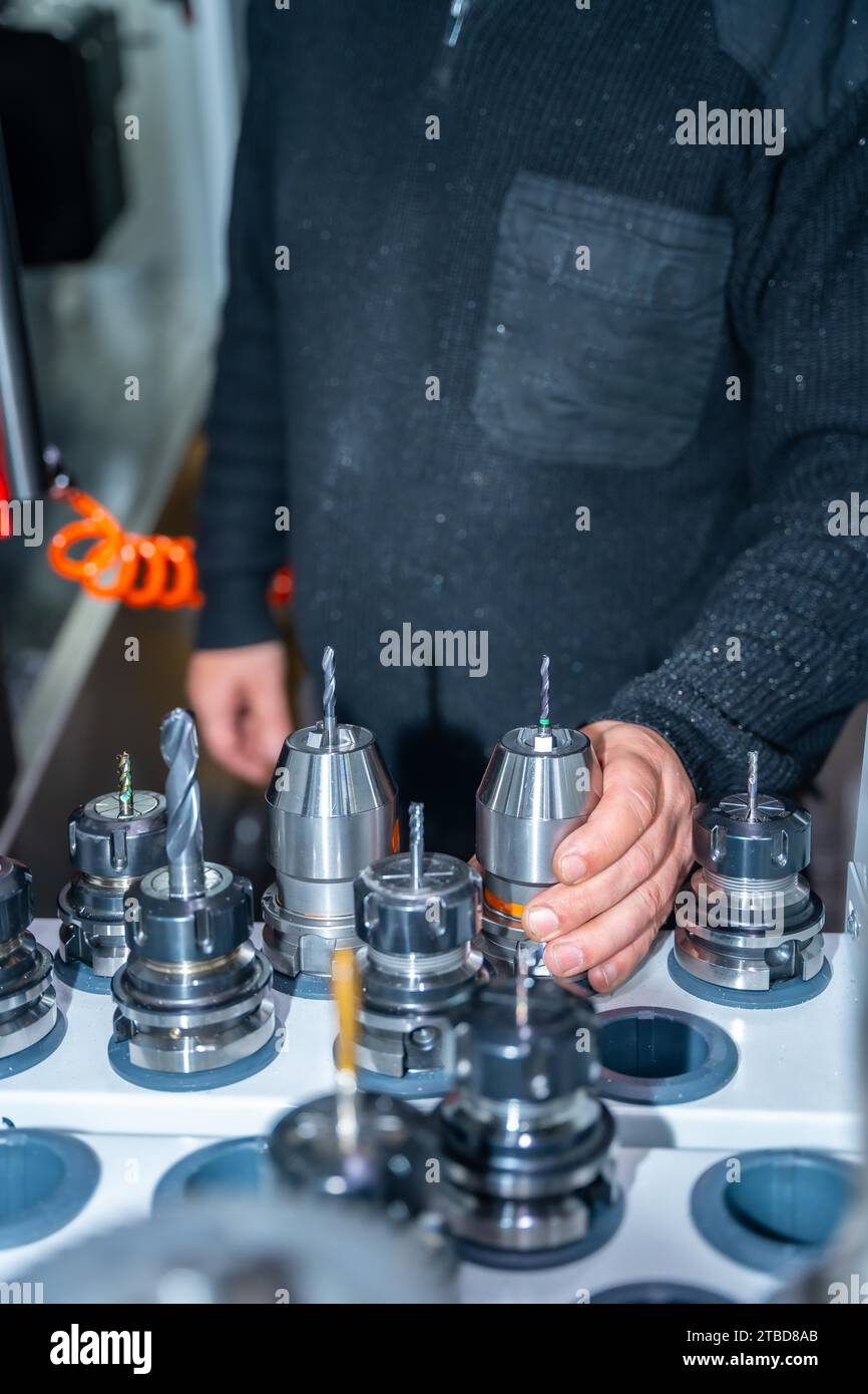 Foto verticale di un lavoratore irriconoscibile che tiene un tornio tra una collezione di torni in una fabbrica cnc Foto Stock