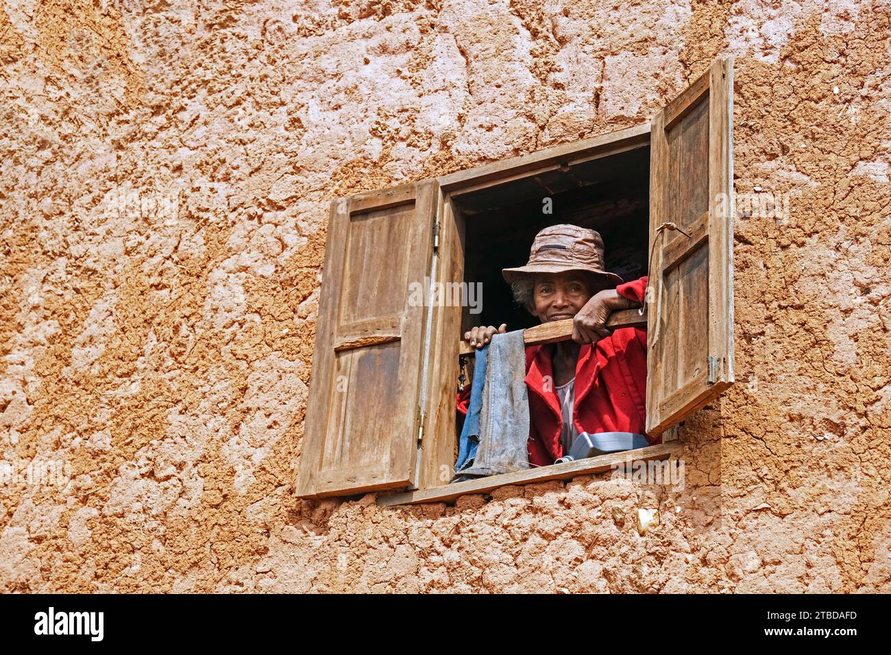 Anziana donna malgascia che guarda dalla finestra in una casa di fango a due piani nel distretto di Ambositra, regione di Amoron'i Mania, Madagascar centrale, Africa Foto Stock