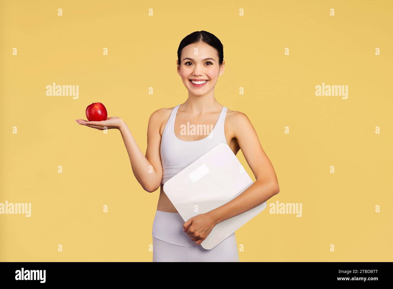 Allegra signora caucasica in abbigliamento sportivo, raccomando mela fresca isolata su sfondo giallo, foto da studio Foto Stock