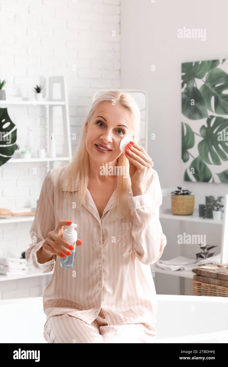 Donna matura che applica il prodotto cosmetico con tampone di cotone in bagno Foto Stock